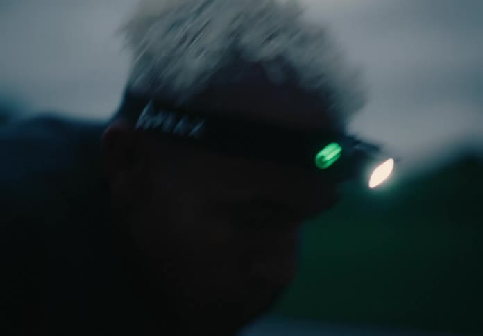 A man wearing a headlamp huffing and breathing heavy as works out at dusk