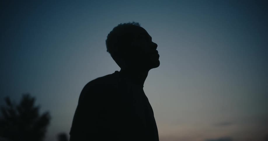 The silhouette of a person standing looking up in a pitch black environment with the sky brightening in the morning