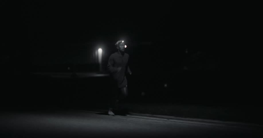 Man in a headlamp runs at the edge of the road in the dark