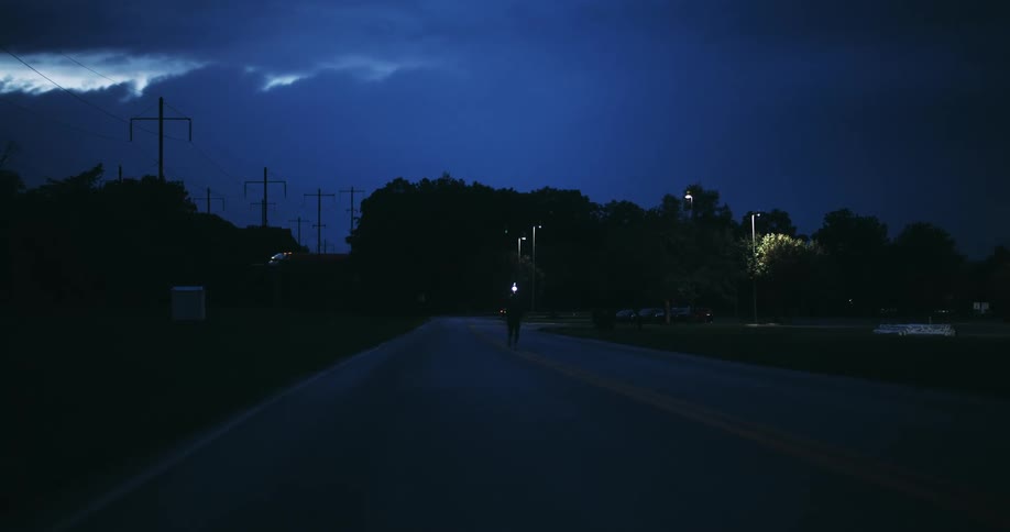 A person wearing a headlamp runs down a dark empty road at night