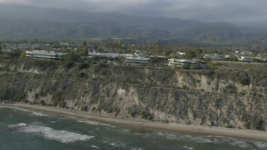 Waves roll up onto a beach below cliffs with buildings on them