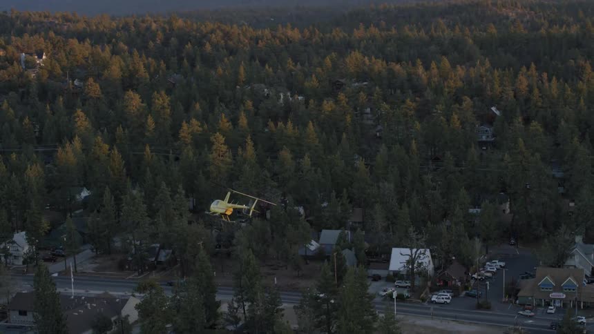 Small helicopter flying above a city street surrounded by trees