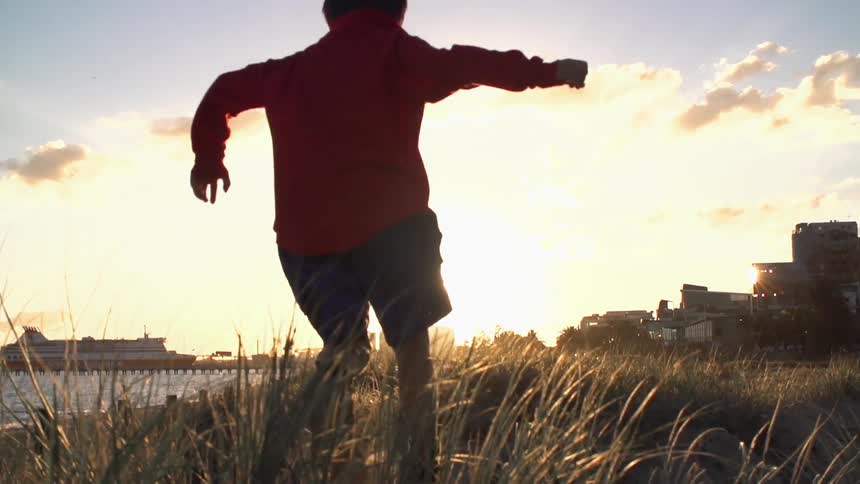 Child runs through the grass by water