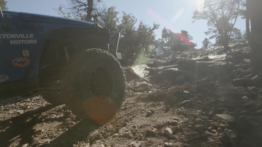 Vehicle climbing a rocky dirt incline on a clear day