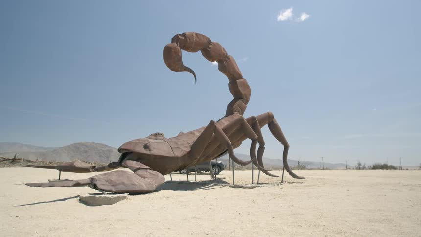 An suv is driving past a large sculpture of a scorpion in the desert