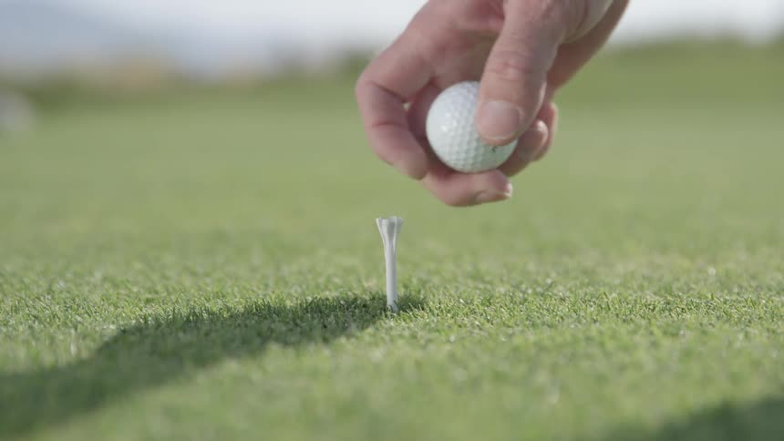 A man is placing a golf ball on a tee