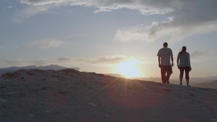 A man and woman walking on a hill at sunset