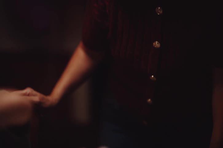 A mother smiles and laughs interacting with her son as he opens a gift in a dimly lit room