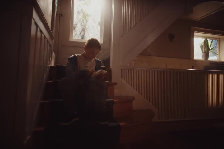 A young boy sits on a staircase reading a letter