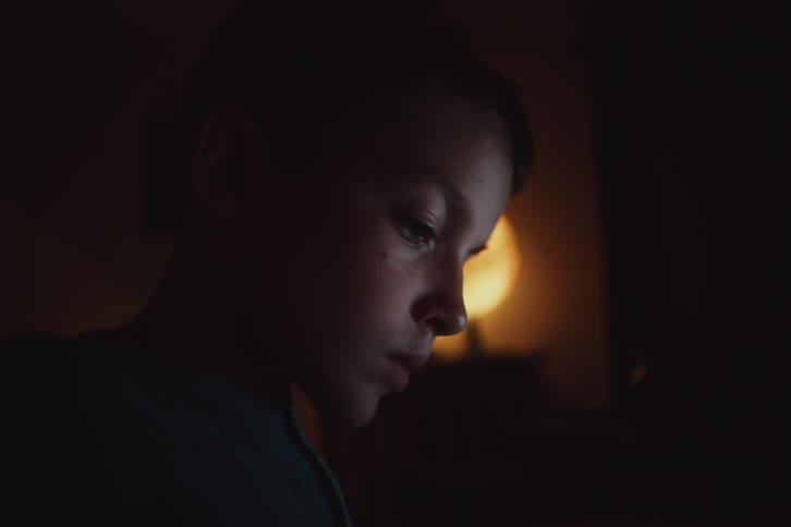 Side portrait of a boy in a dark room concentrating