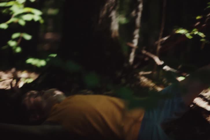 A little boy in an orange tank top lies on the ground next to a tree in the forest and he is happy