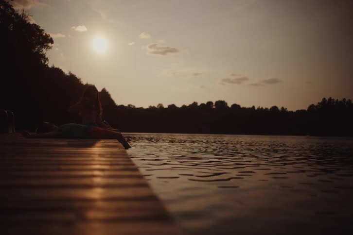 A child lies on a dock and dips their toes into the lake