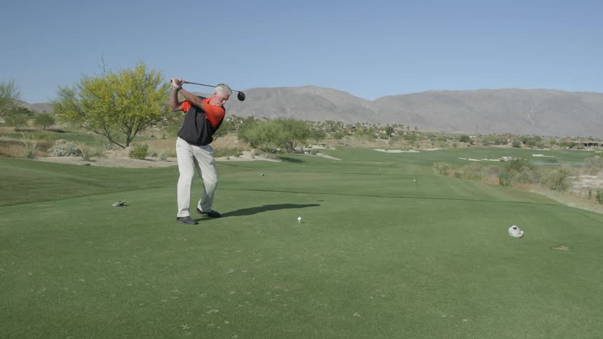 A man swings a golf club to hit a ball down the fairway