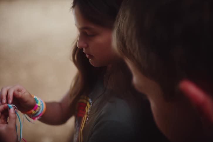 A young girl teaches a boy how to make a friendship bracelet