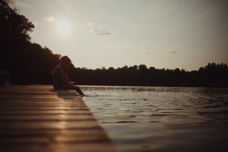 Two children are sitting on the pier kicking their feet in the water