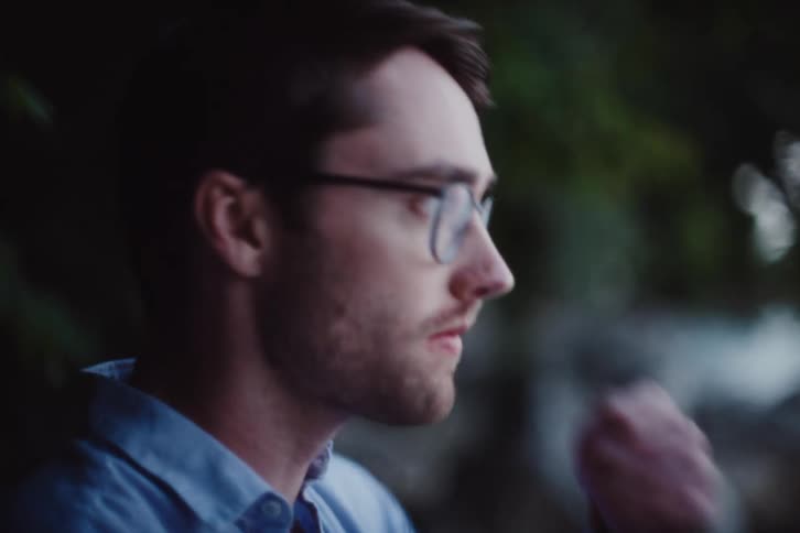 The face of a man with glasses who is finishing chewing something and puts his hand over his mouth