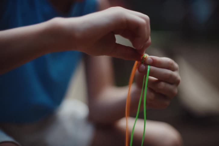 With focused fingers the person carefully knots together vibrant strands of thread