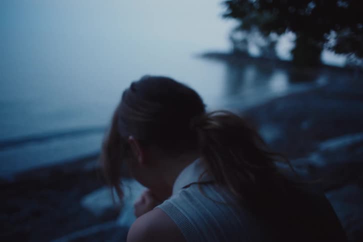 A woman with a ponytail and sleeveless shirt laughs by the lake