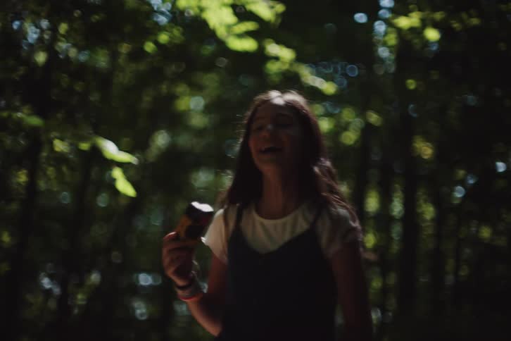 A girl takes a picture of a boy in the woods
