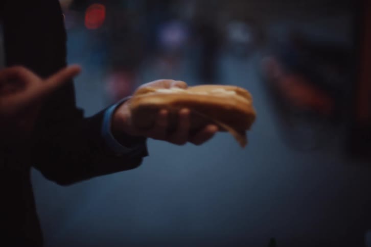 Man wearing glasses and a blazer jacket is squeezing mayonnaise onto his sandwich