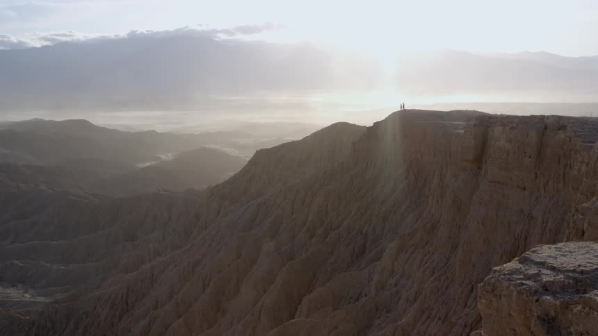 Two people standing at the edge of a cliff on a sunny day