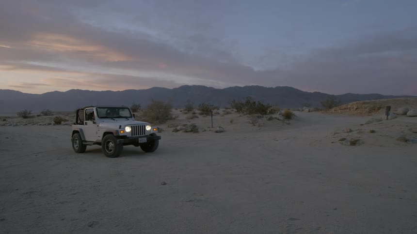A jeep rides in the desert at sunset