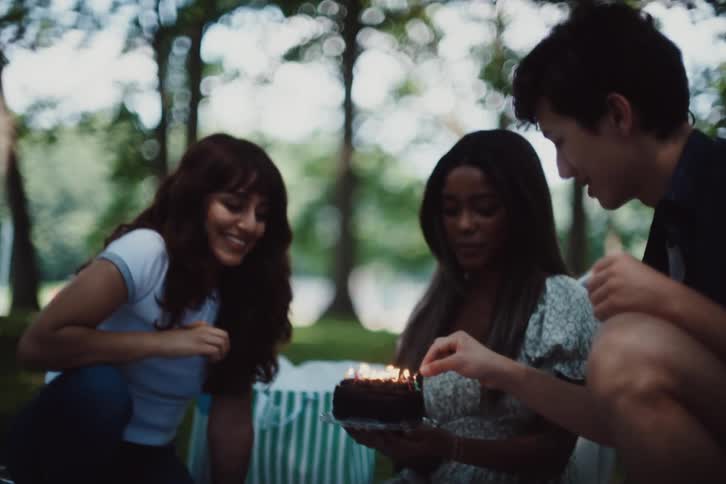 Group of friends sitting on the grass lighting birthday candles on a cake