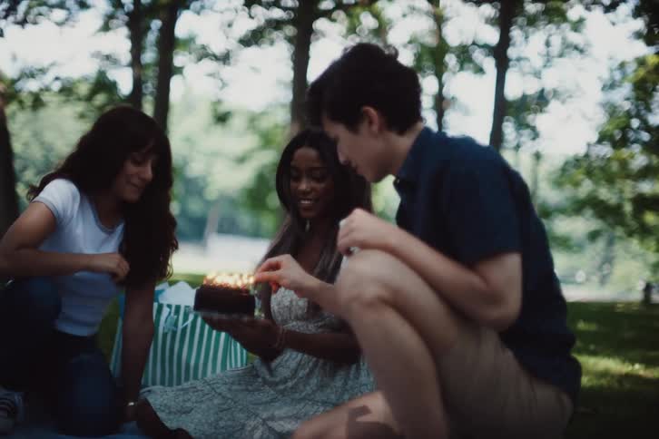Birthday girl holds her cake while the candles are lit by a friend during a picnic in the park