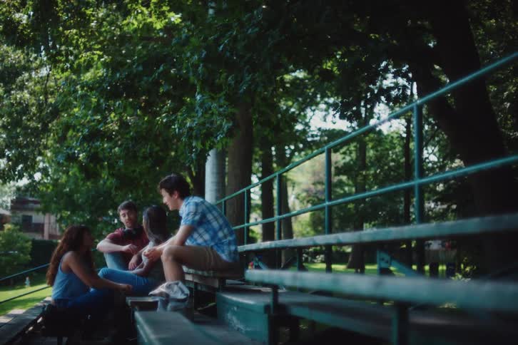 A small group of friends sits on the bleachers at a park and talk amongst one another