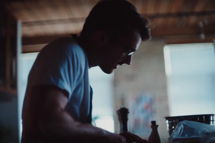 A man wearing an apron chops up something with a knife on his kitchen counter