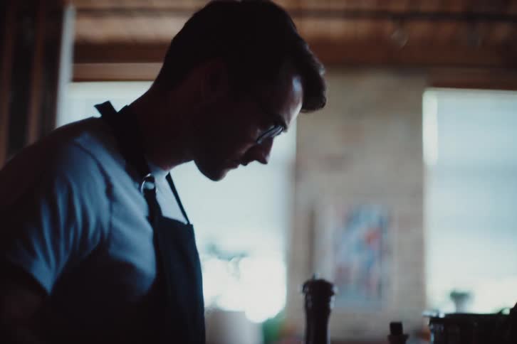 A man wearing an apron cuts food with a knife in a kitchen