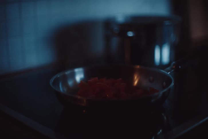 Person cooking in the kitchen seasons food in a skillet on the stove top