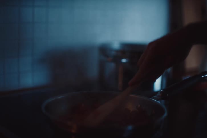 A close up of a pan on a stovetop with food being cooked and steam rising in a dimly lit kitchen
