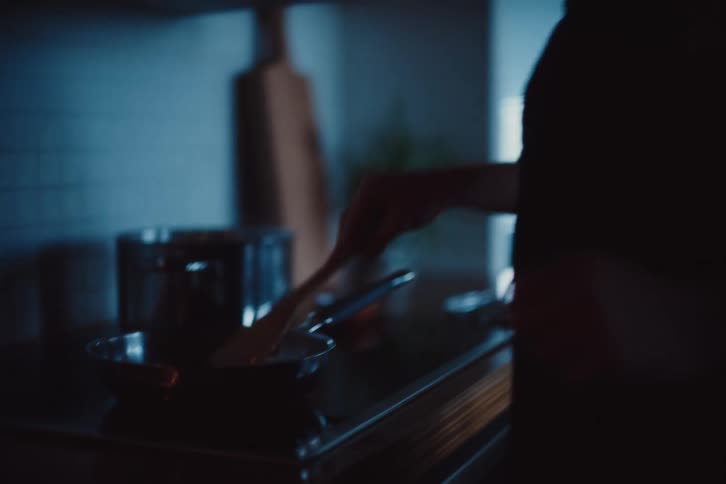A man wearing an apron sautes something in a pan on a stove in his kitchen