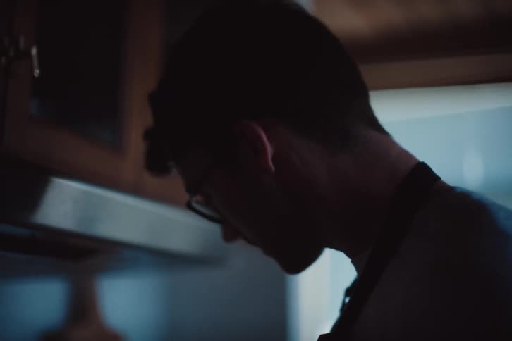 A young man using a wooden spoon to stir food that is cooking in a pan