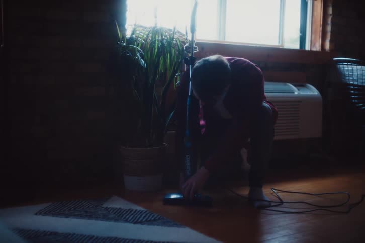 A person is crouched on the floor fixing a vacuum cleaner
