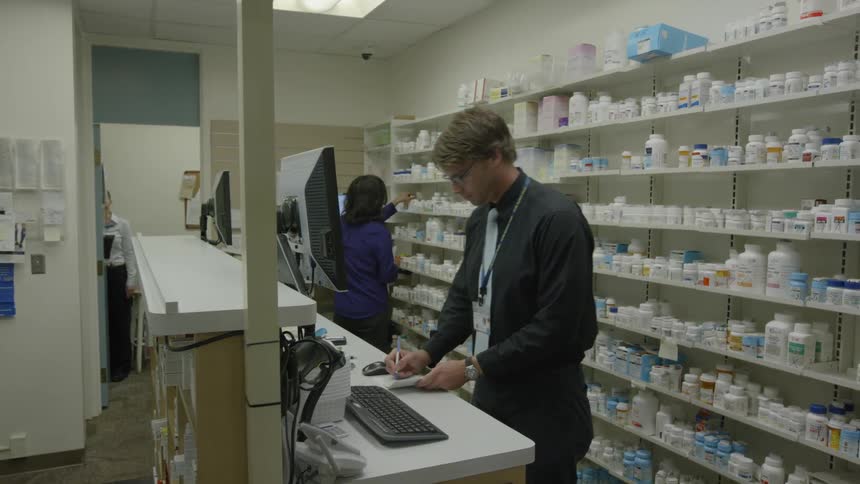 A man stands at a computer in a pharmacy