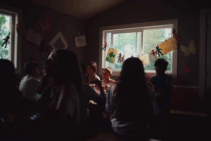 Several children gathered around a large table and some of them are eating and talking