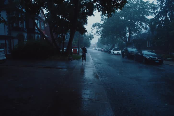 An adult walks down the sidewalk in a suburb in the pouring rain