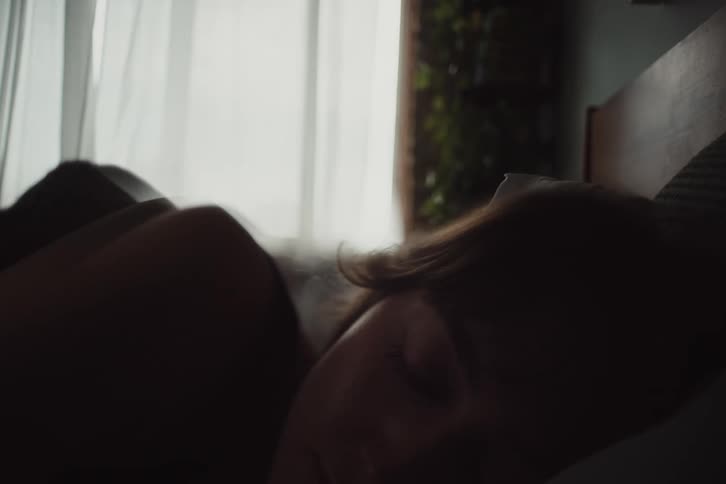 A peaceful scene of a person sleeping in soft light near a window with sheer curtains