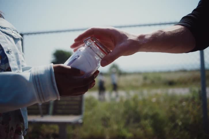 Woman picking up a small glass jar with letters and handing it to a man and they both hug