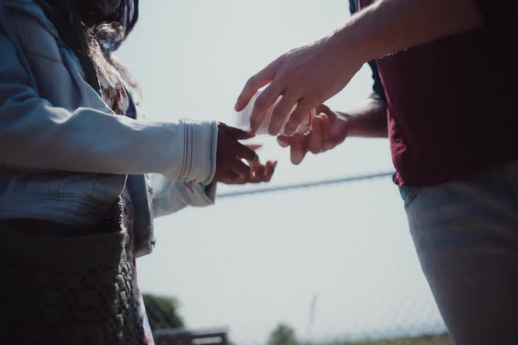 A woman takes a glass bottle out of her bag and gives it to a man in front of her and they hug