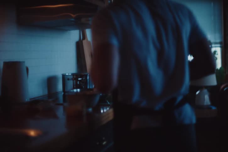 A man starts cooking food on a stove in a darkened kitchen