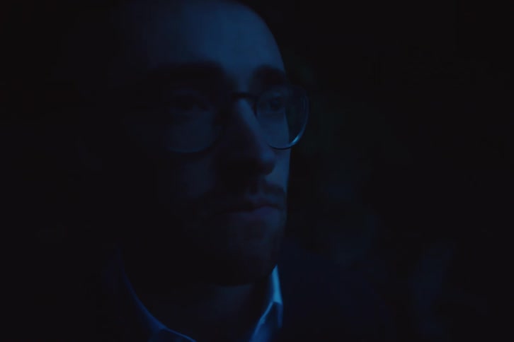 The face of a man with glasses and he is chewing while looking forward and it is night