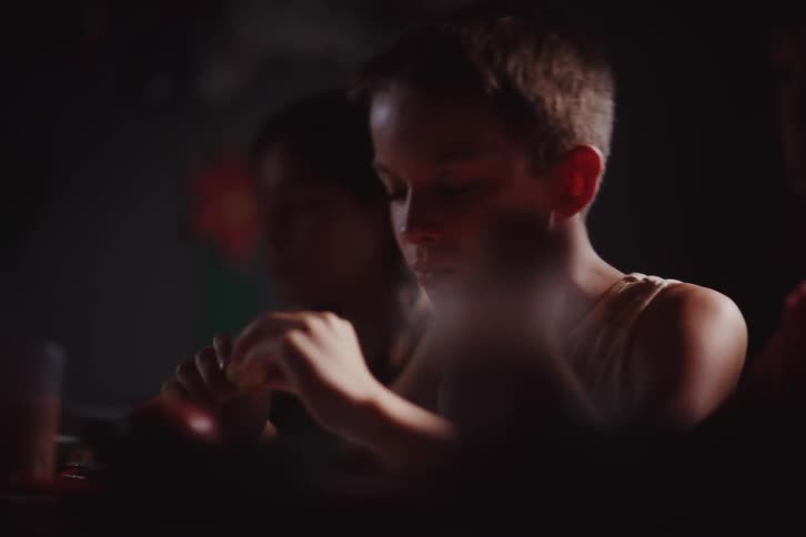 A young boy eating in soft dim light with a thoughtful and focused expression