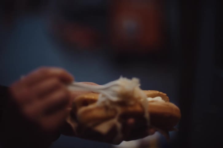 A man puts toppings on his hot dog