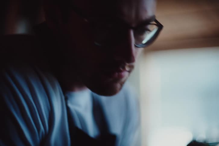 The man clad in a blue shirt and framed by glasses focuses his gaze downward