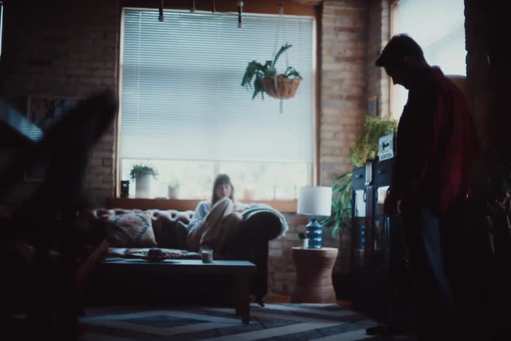 Woman sitting on the sofa in the living room and a man vacuuming the carpet