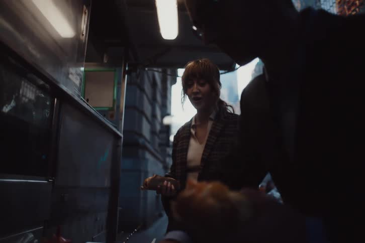 Man and a woman seasoning a hot dog in a food truck on the sidewalks of a city