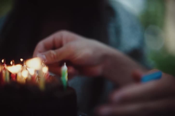 A persons hands are lighting candles on a birthday cake